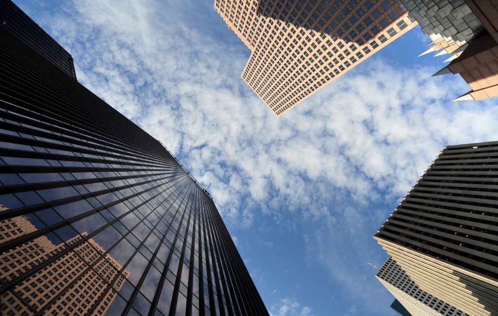 Skyscrapers rising into a cloudy blue sky seen from street level.