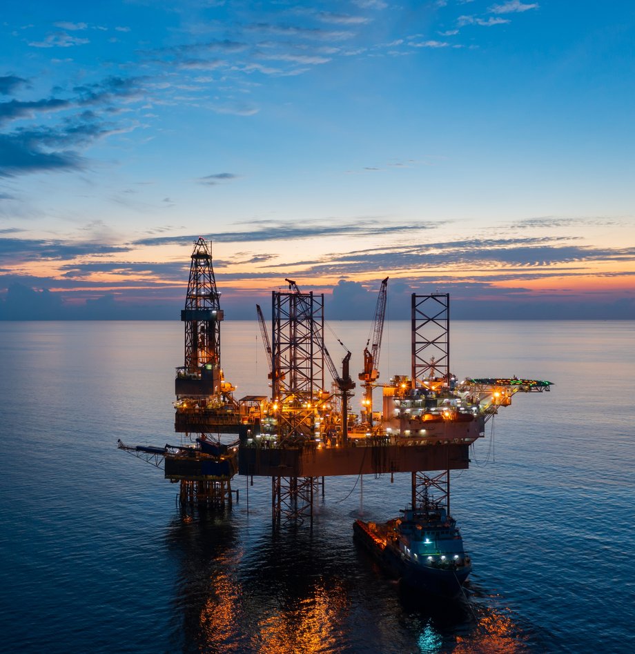 Offshore oil drilling platform lit up on the sea at sunset.